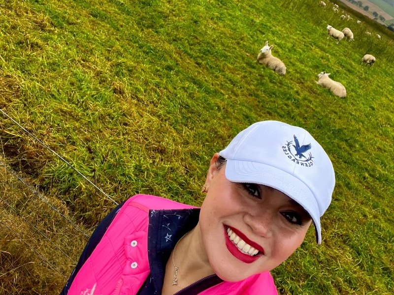 Jessica Villarreal on a grassy hillside in Scotland with sheep grazing behind her